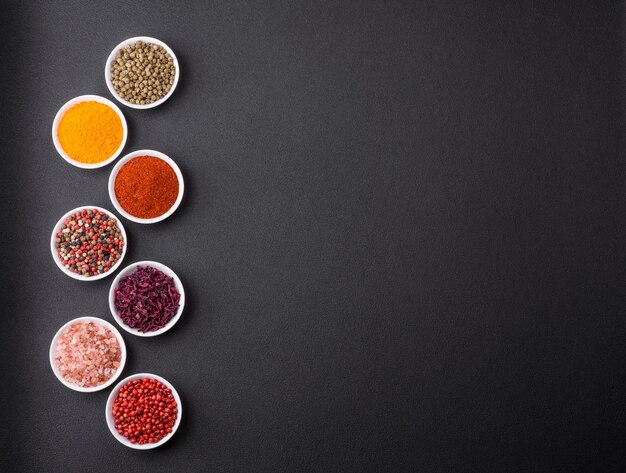 Photo composition consisting of a variation of several types of spices in white ceramic bowls on a textured concrete background