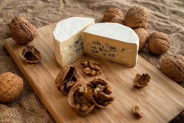 Composition of a cut cheese head with white and green mold and walnuts on a bamboo board on a backgr