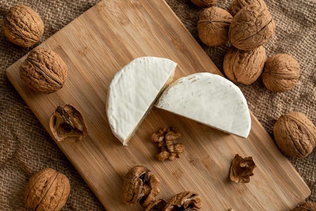 Composition of a cut cheese head with white and green mold and walnuts on a bamboo board on a backgr