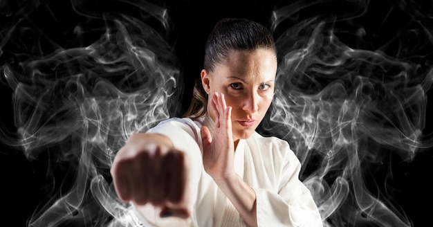 Composition of female martial artist over trails of smoke on black background