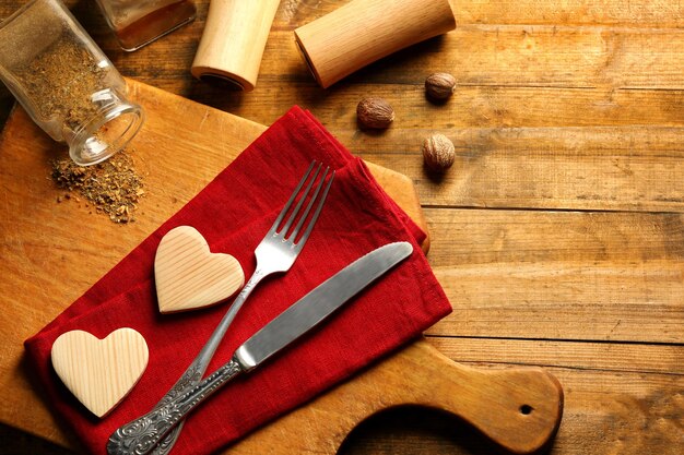 Composition of fork knife napkin and decorative hearts on cutting board on wooden table background