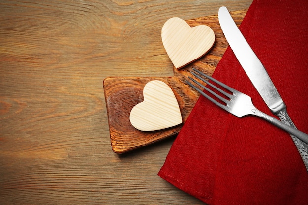 Composition of fork knife napkin and decorative hearts on cutting board on wooden table background