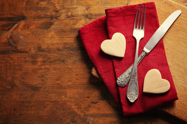 Composition of fork knife napkin and decorative hearts on cutting board on wooden table background