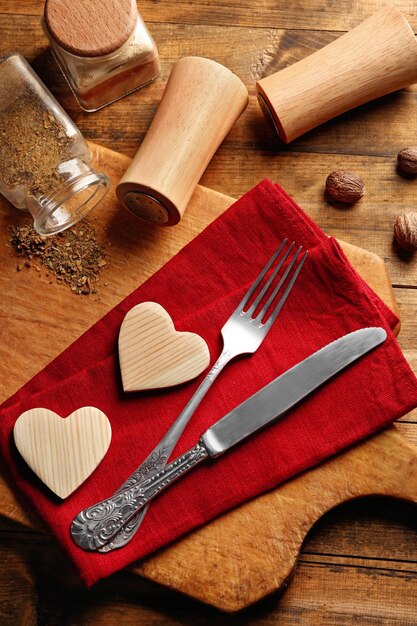 Composition of fork knife napkin and decorative hearts on cutting board on wooden table background