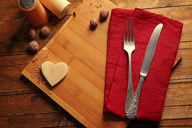 Composition of fork knife napkin and decorative hearts on cutting board on wooden table background