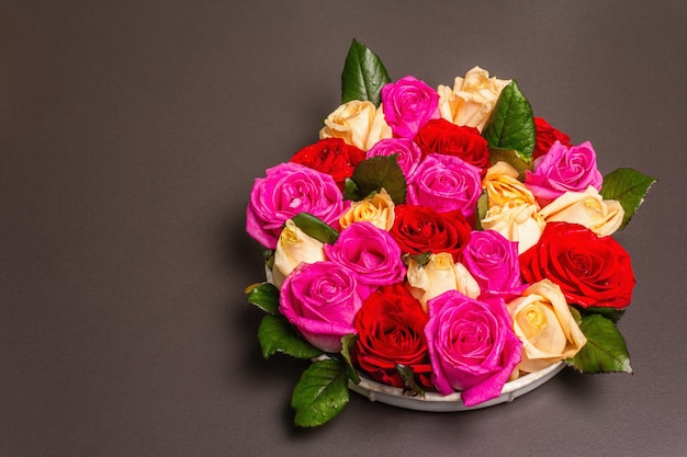 Composition of fresh multicolored roses on ceramic stand. The festive concept for Weddings, Birthdays, March 8th, Mother's, or Valentine's Day. Greeting card, flat lay, black stone background