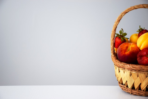 Photo composition of fresh ripe juicy fruits and berries: peaches, strawberry and apricots in wicker basket