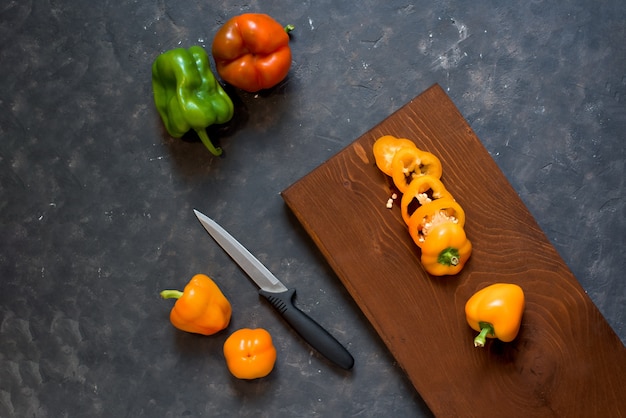 Состав свежих овощей нарезанный перец на доске на темный и весь перец оранжевый. вид сверху .