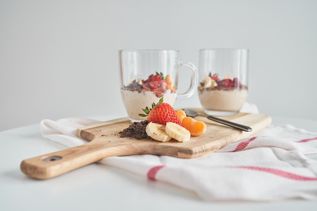 Composition of fresh yogurt with grated chocolate and sliced banana mandarin and strawberry placed on cutting board on white napkin