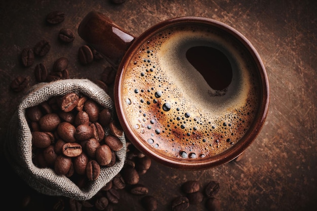 Composition of freshly brewed cup of coffee and roasted coffee beans in bag on brown background