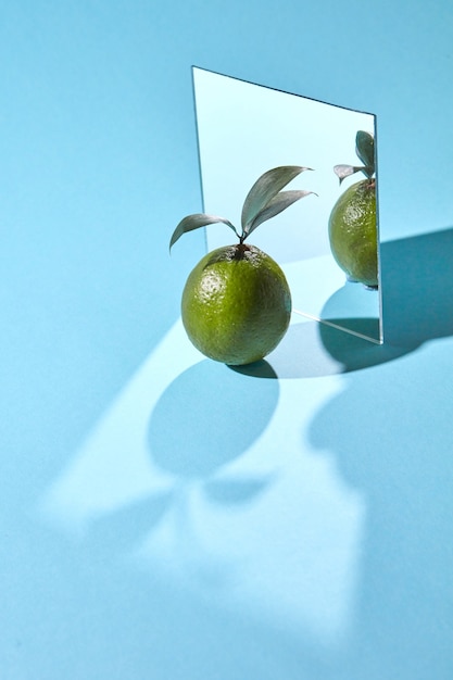 Фото Композиция из зеркала и лайма с листьями на синем фоне с отражением теней и копией пространства. органические фрукты