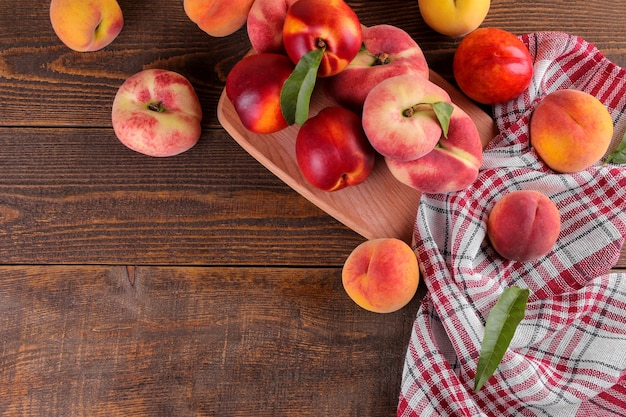 A composition from many varieties of peach on a cutting board on a brown wooden background with a place for an inscription. Top view