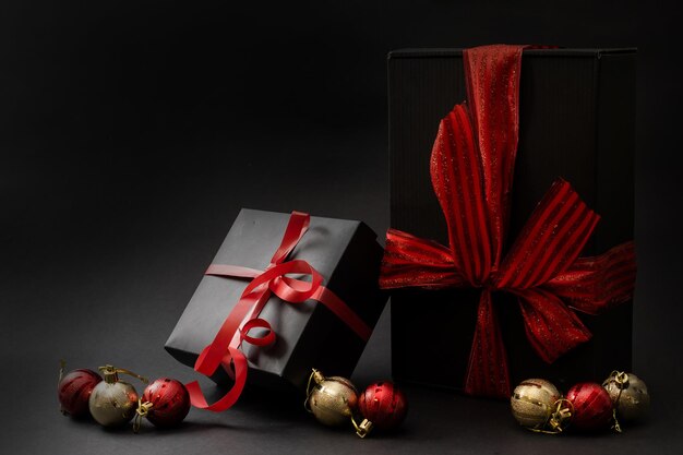 Composition of gifts of different shapes wrapped in black wrapping paper with a red ribbon and a bow on a black background. Side view. Copy space.