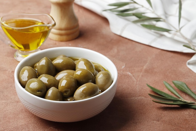 Composition of green olives in oil, olive branch, gravy boat on the background. Space for text.