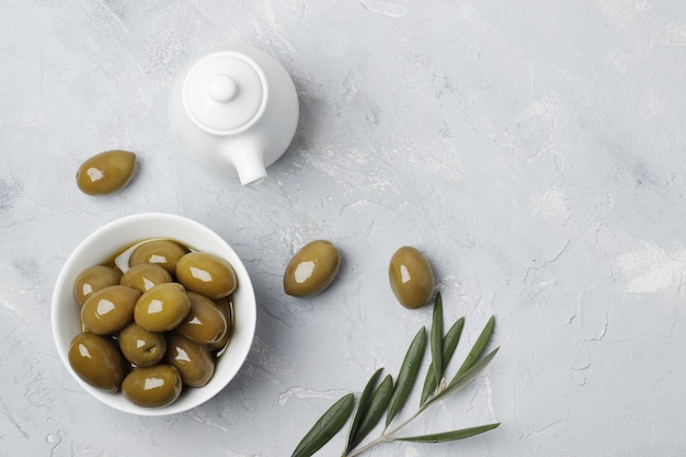 Composizione di olive verdi, olio, spezie, salsiere, su sfondo bianco.