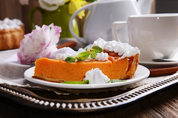 Composition of homemade pumpkin pie on plate and flowers in vase on wooden background