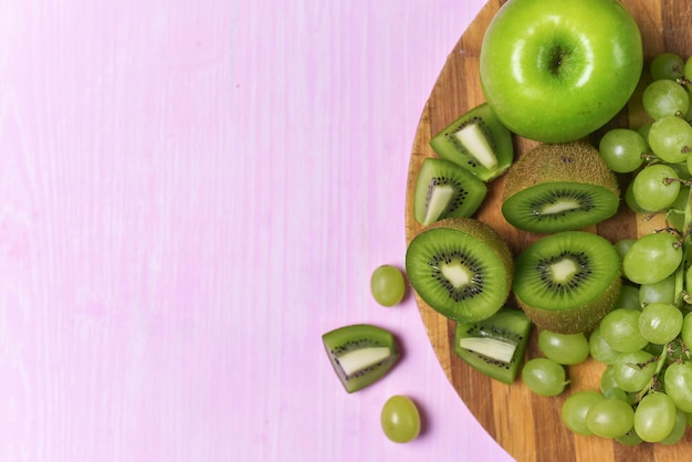 Composition of kiwi, grape and apple on a pink background