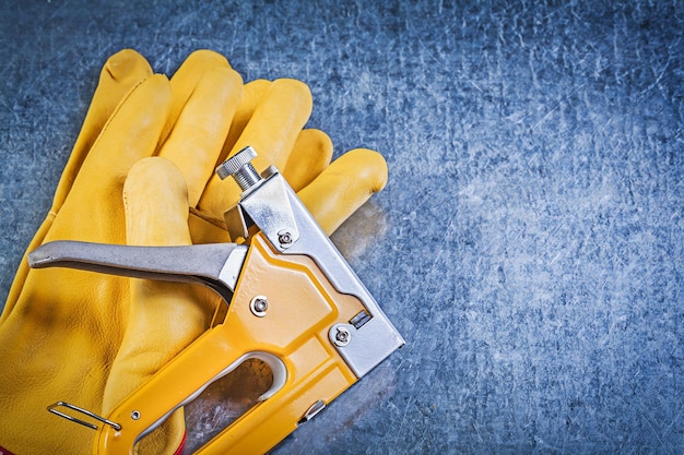 Composition of leather safety gloves staple gun on metallic background construction concept