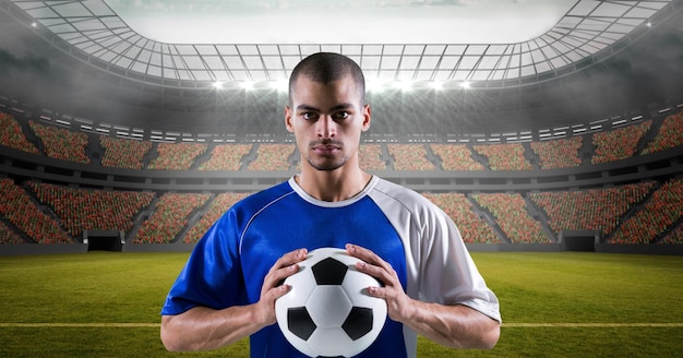 Состав мужского футболиста, держащего футбол над спортивным стадионом