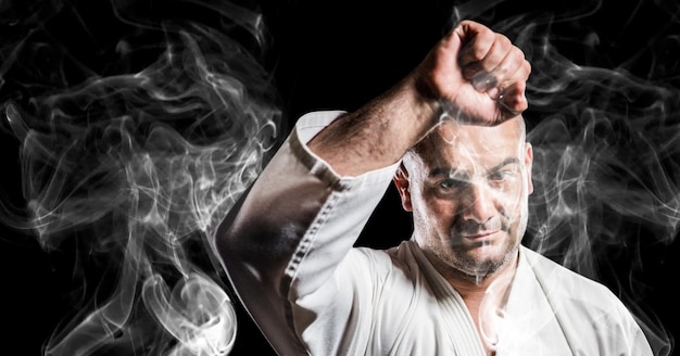 Composition of male martial artist over trails of smoke on black background