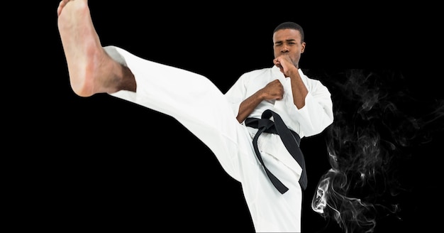 Composition of male martial karate artist with black belt kicking over smoke and copy space