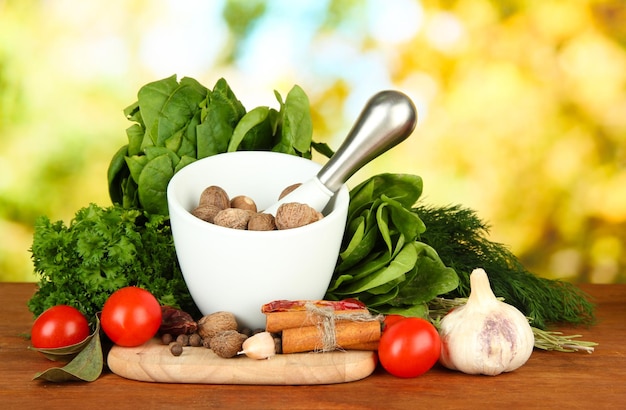 Composition of mortar spices tomatoes and green herbs on bright background