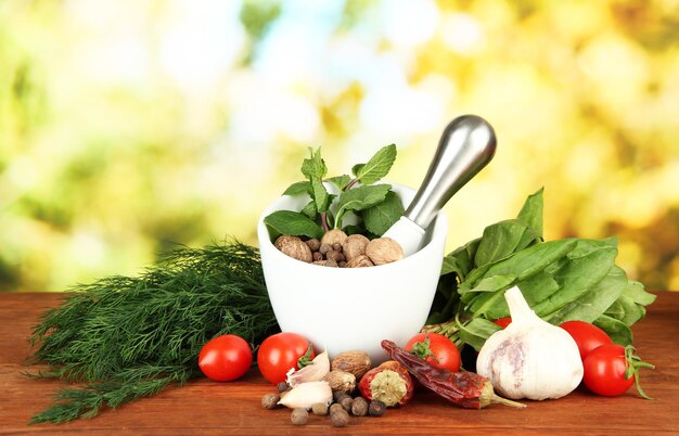 Composition of mortar spices tomatoes and green herbs on bright background