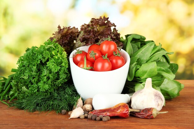 Composition of mortarspices tomatoes and green herbs on bright background