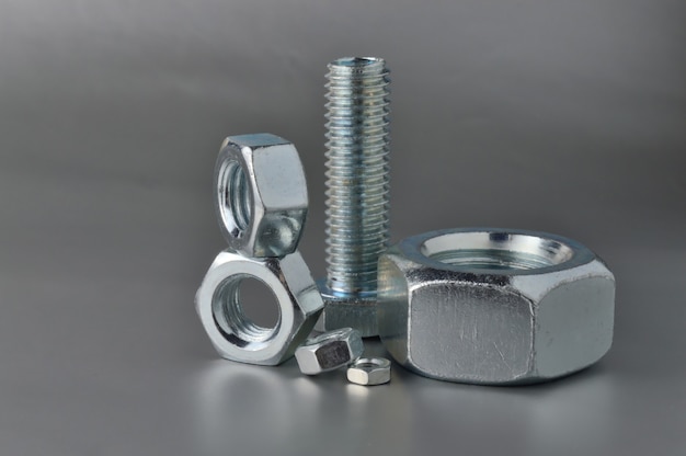 Composition of new bolts and nuts of different sizes on a gray background.