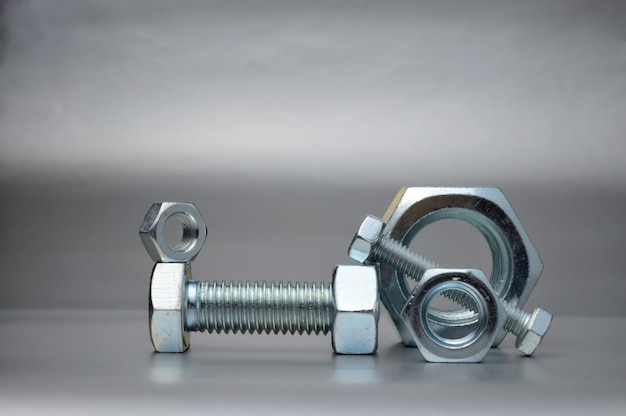 Composition of new bolts and nuts of different sizes on a gray background.