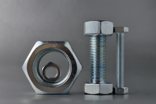 Composition of new bolts and nuts of different sizes on a gray background.