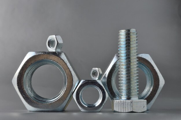 Composition of new bolts and nuts of different sizes on a gray background.