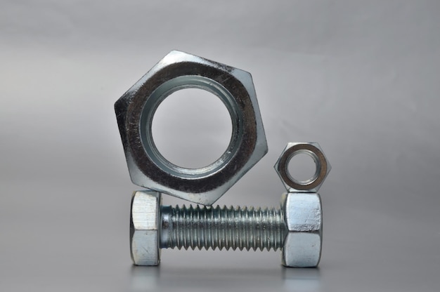 Composition of new bolts and nuts of different sizes on a gray background.