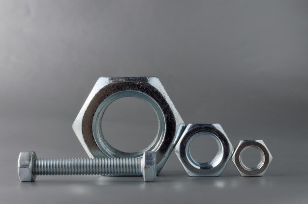 Composition of new bolts and nuts of different sizes on a gray background.