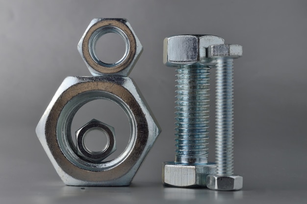 Composition of new bolts and nuts of different sizes on a gray background.