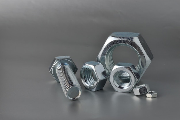 composition of new bolts and nuts of different sizes on a gray background.