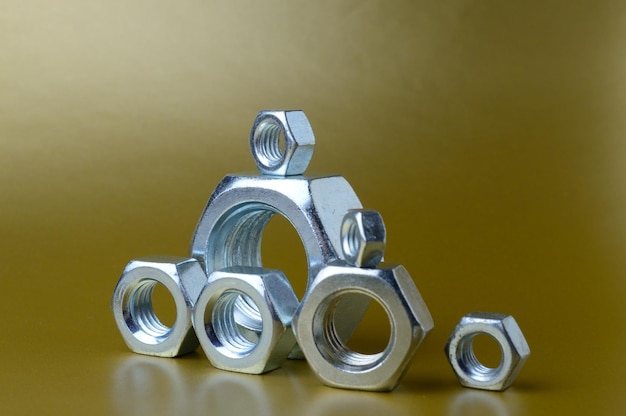 Composition of new nuts and bolts of different sizes on a yellow background