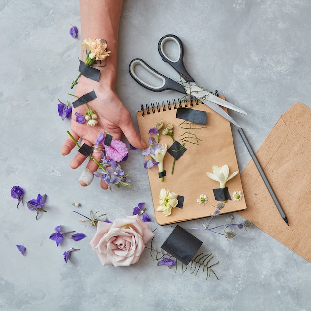 Composition of notebook, human being's hand with pencil, scissors and many flowers for decorating or designing copy space in Valentine's Day, wedding, Woman's Day.