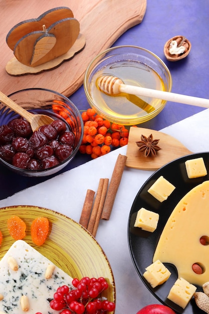 Состав из двух видов сыров с орехами, ягодами и фруктами на черных и желтых тарелках сыры с медом на бело-голубом фоне крупным планом