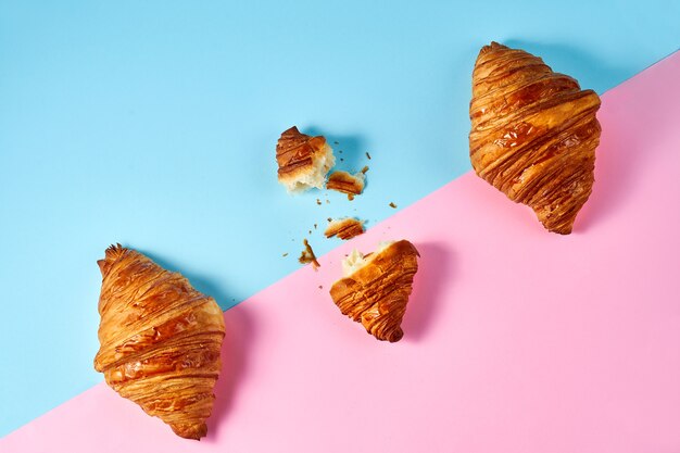 Composition-pattern with 3 croissants and one broken on a blue and pink background.