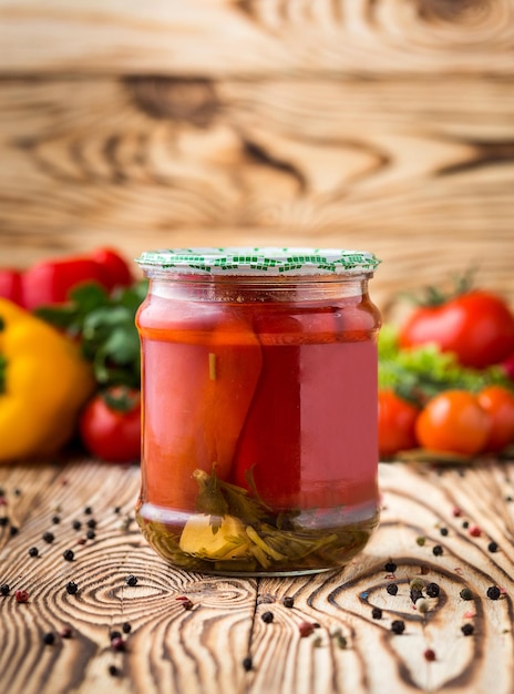 Composition of pickled pepper in jar and ingredients on wooden background