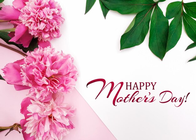 Composition of pink peonies, leaves on a white and pastel pink background. Fresh flowers. Inscription Happy Mother's Day. Banner, poster for Mother's Day. Flat lay, top view, close up, copy space