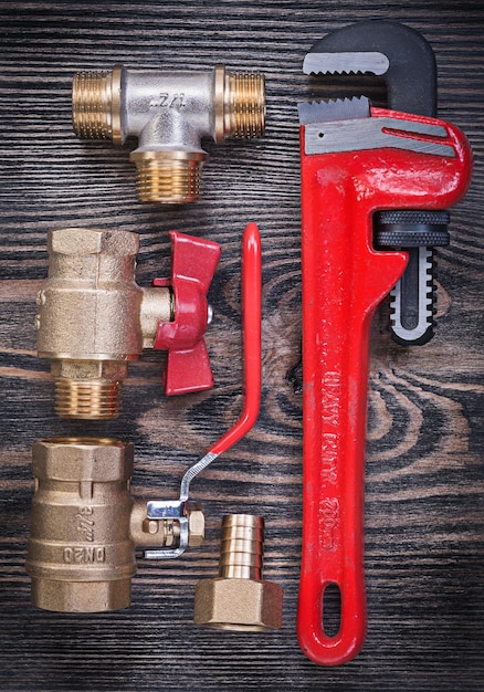 Composition of pipe wrench brass fittings water valve on wood board plumbing concept.