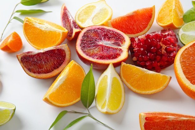 Composition of pomegranate and citrus fruits with green leaves on white background