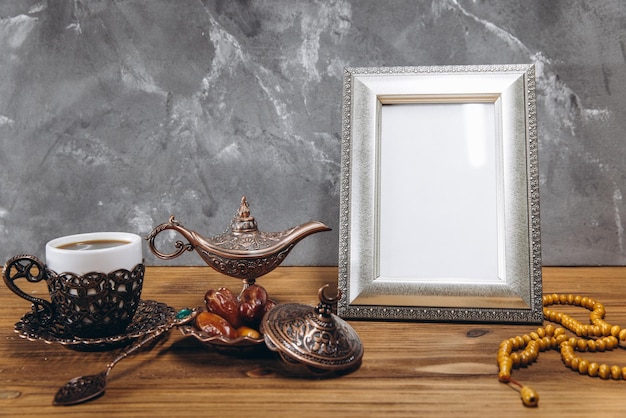 Composition for Ramadan Silver frame with copy space or mockup near traditional islamic tableware with dates and coffee on wooden table