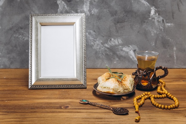 Composition for Ramadan Silver frame with copy space or mockup near traditional islamic tableware with dates and tea on wooden table