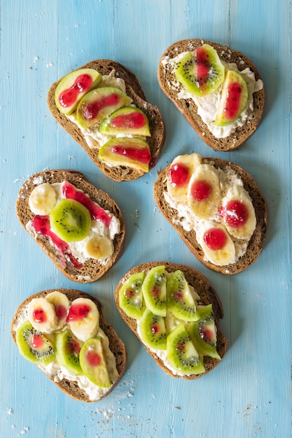 Composition sandwiches with fruit cream banana apple and kiwi on a blue wooden background