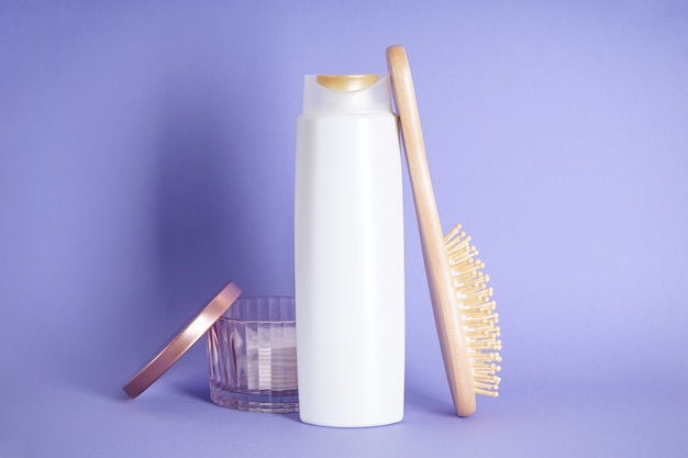 Composizione della bottiglia di shampoo e una spazzola per capelli in legno su uno sfondo viola.