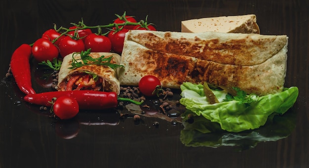 Composition of shawarma red pepper cherry tomatoes cabbage cheese on a black wood background