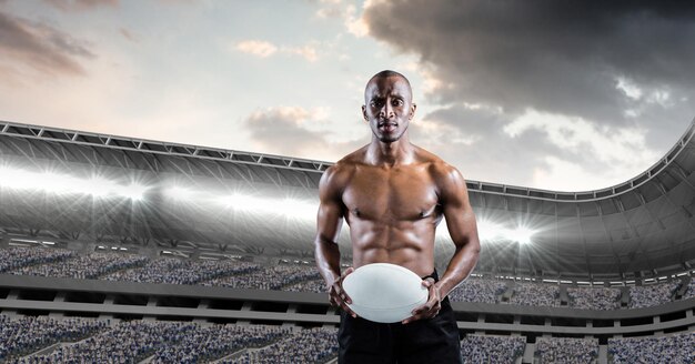 Composition of shirtless male rugby player holding rugby ball over sports stadium